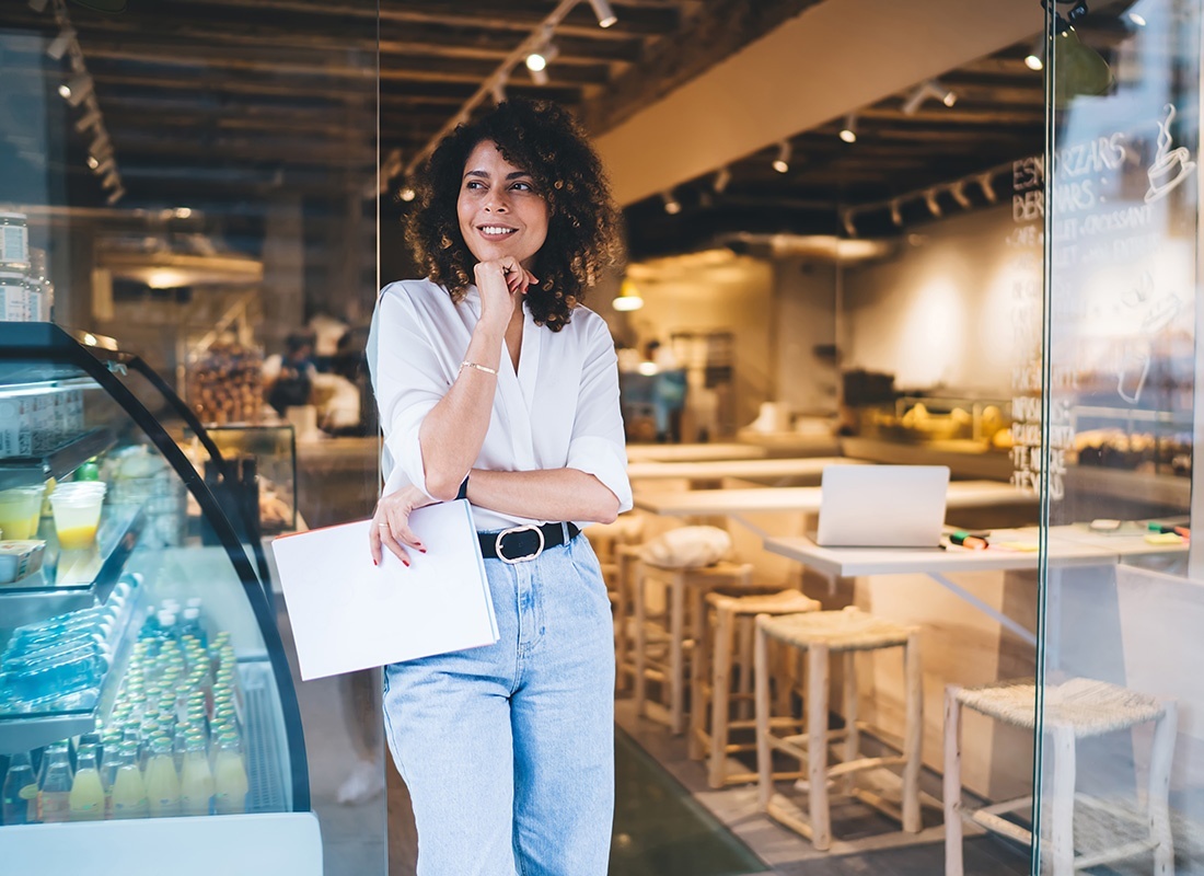 Business Insurance - Portrait of a Smiling Young Female Small Business Owner Holding Pieces of Paper in her Hands as she Stands Outside her Cafe