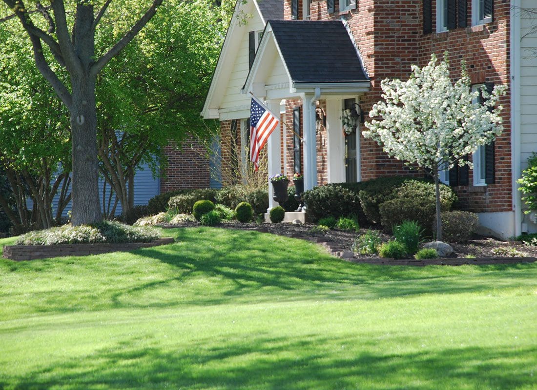 Chester, NY - View of the Front of a Two Story Brick Home with Green Grass and an American Flag Hanging on the Front Entryway in Chester New York