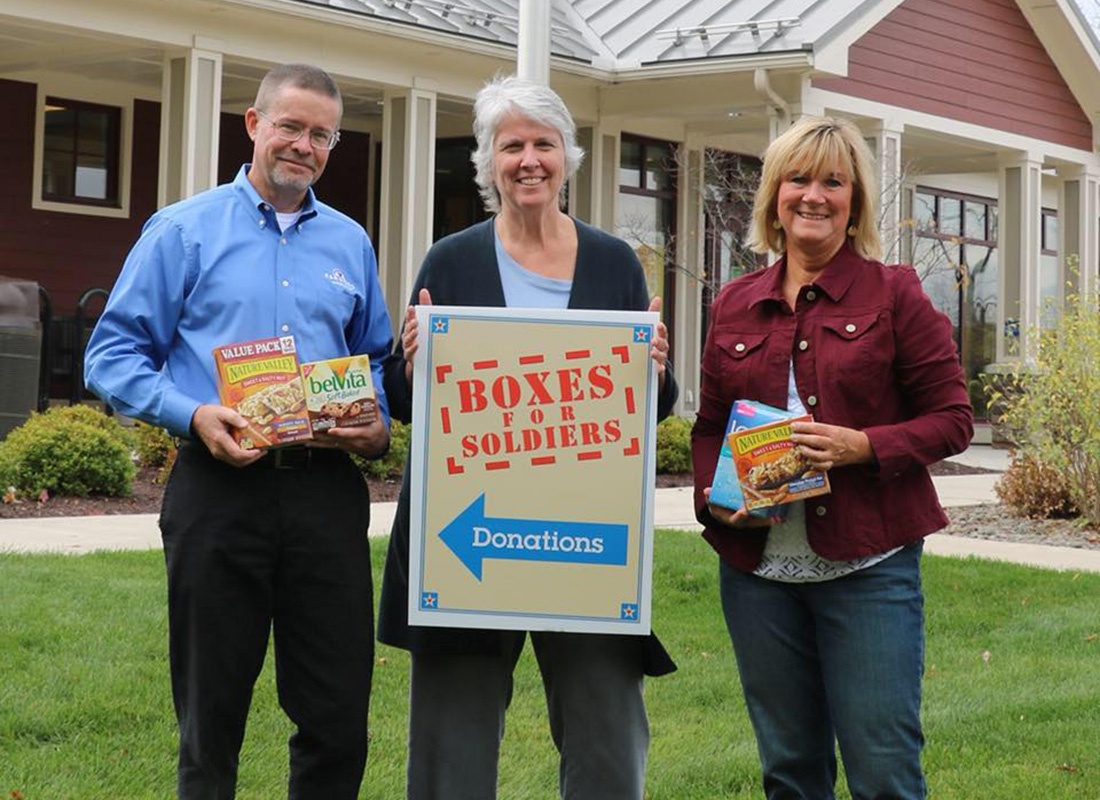 Community Involvement - Portrait of Agency Owner Rob Donating Boxes of Snacks to Boxes for Soldiers While Standing Next to Two Smiling Women