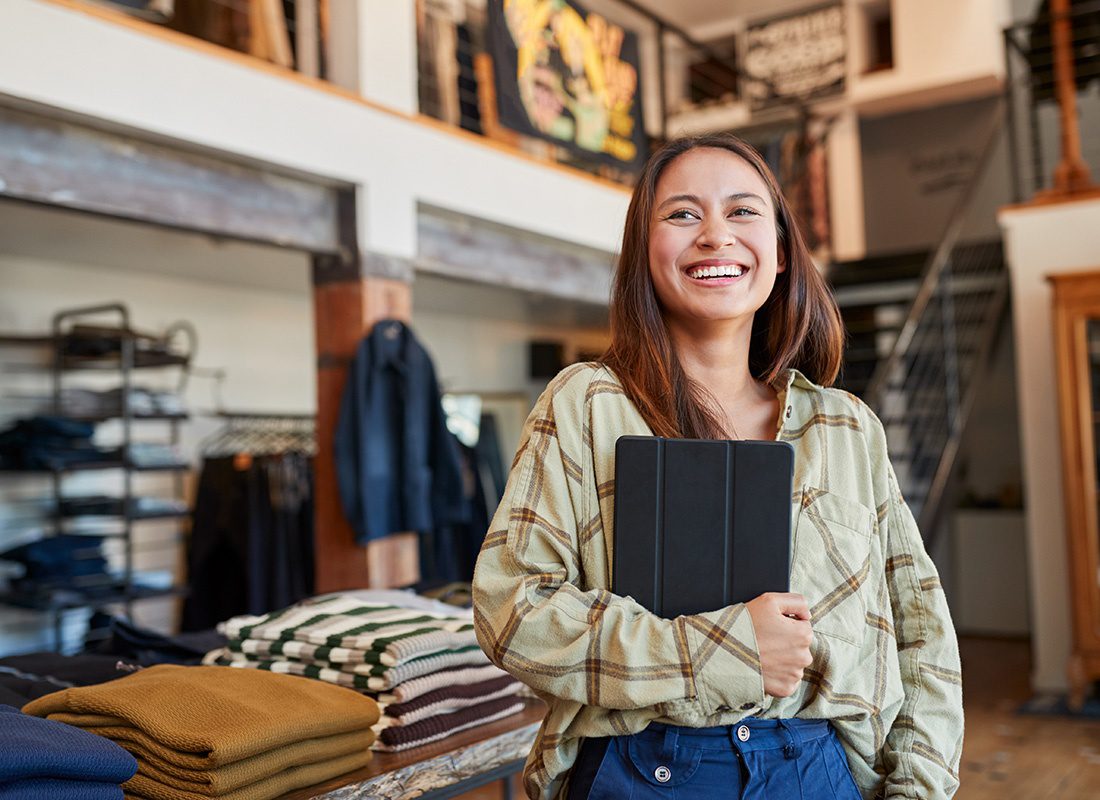Contact - Cheerful Young Female Business Owner Standing in her Clothing Store While Holding a Tablet in her Hand