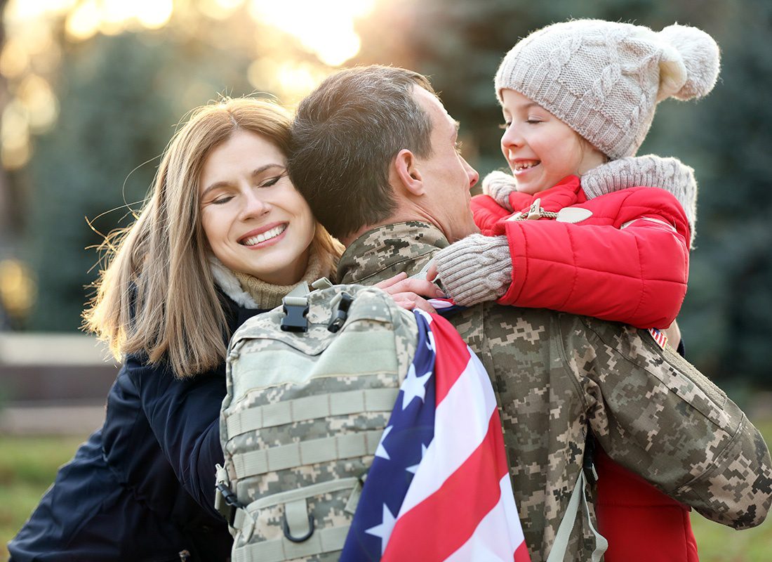 Insurance Solutions - Portrait of a Cheerful Young Daughter and her Mother Hugging her Father in an Army Uniform After Coming Back Home from Deployment