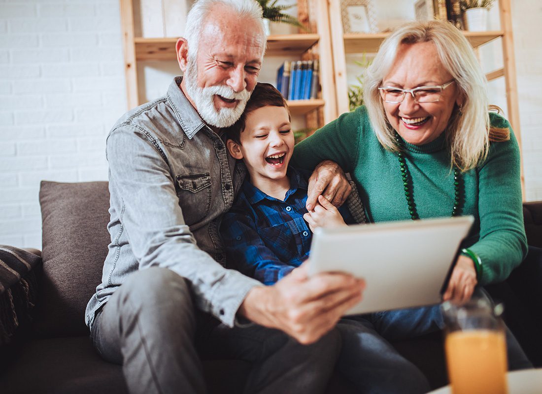 We Are Independent - Portrait of Cheerful Grandparents Sitting with Their Grandson on the Sofa While Having Fun Using a Tablet Together